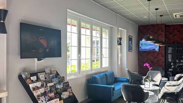 Un área de espera moderna con un sofá azul, sillas negras, un televisor y un mueble para revistas.