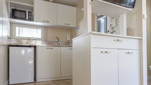 Una cocina compacta con armarios blancos, microondas y televisor integrado.