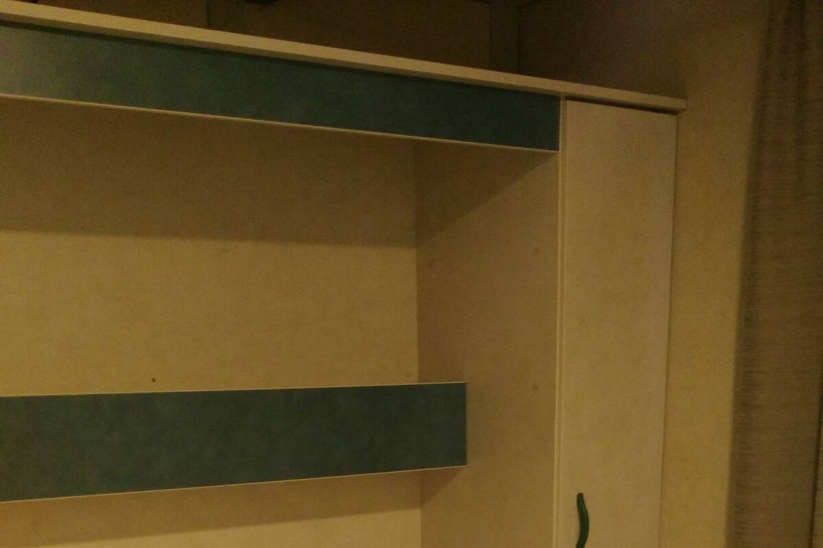 Un lit simple avec une couverture marron et deux serviettes pliées, une armoire en bois et un petit meuble.