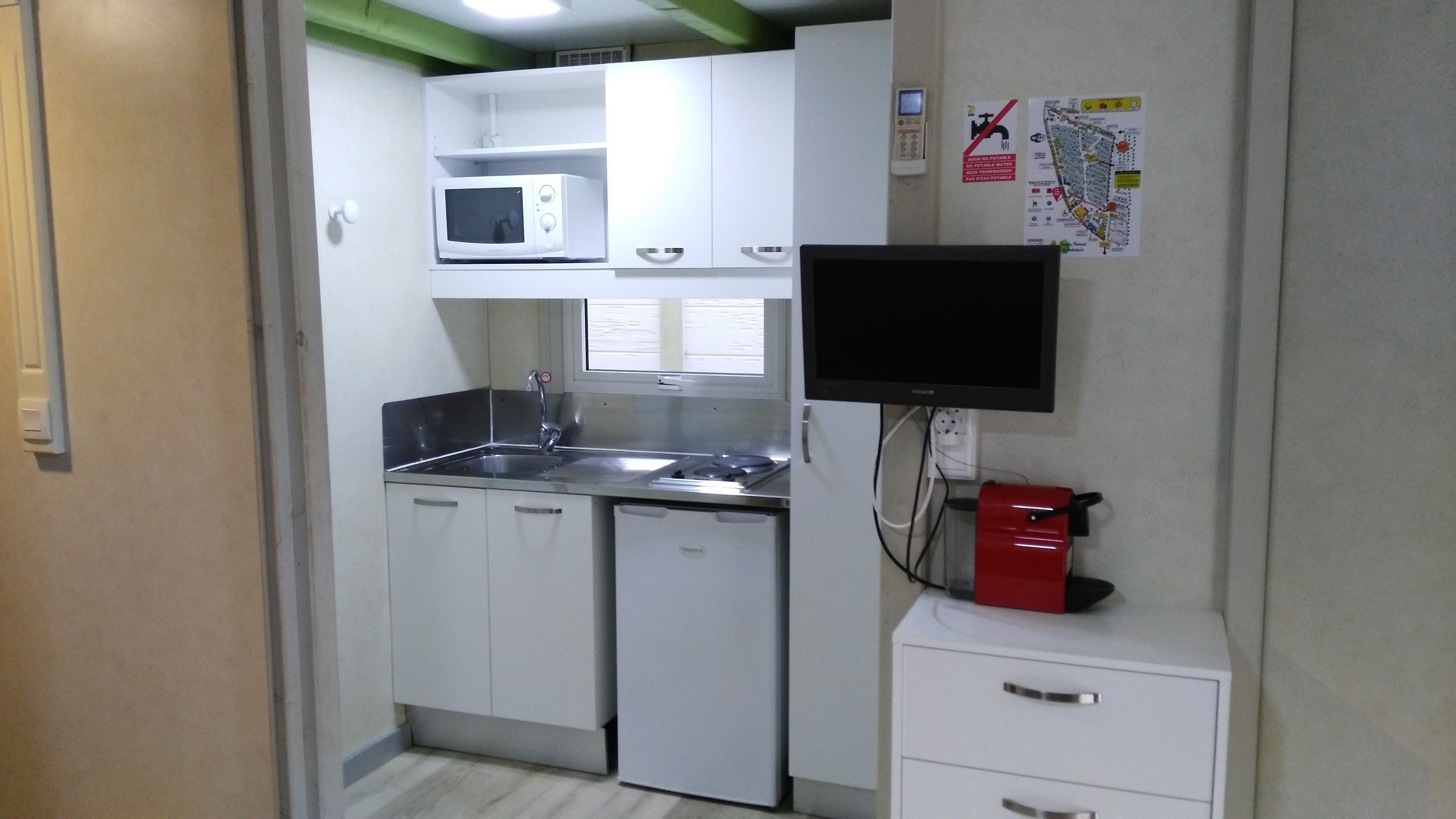Cocina compacta con armarios blancos, microondas, pileta, estufa y heladera pequeña.
