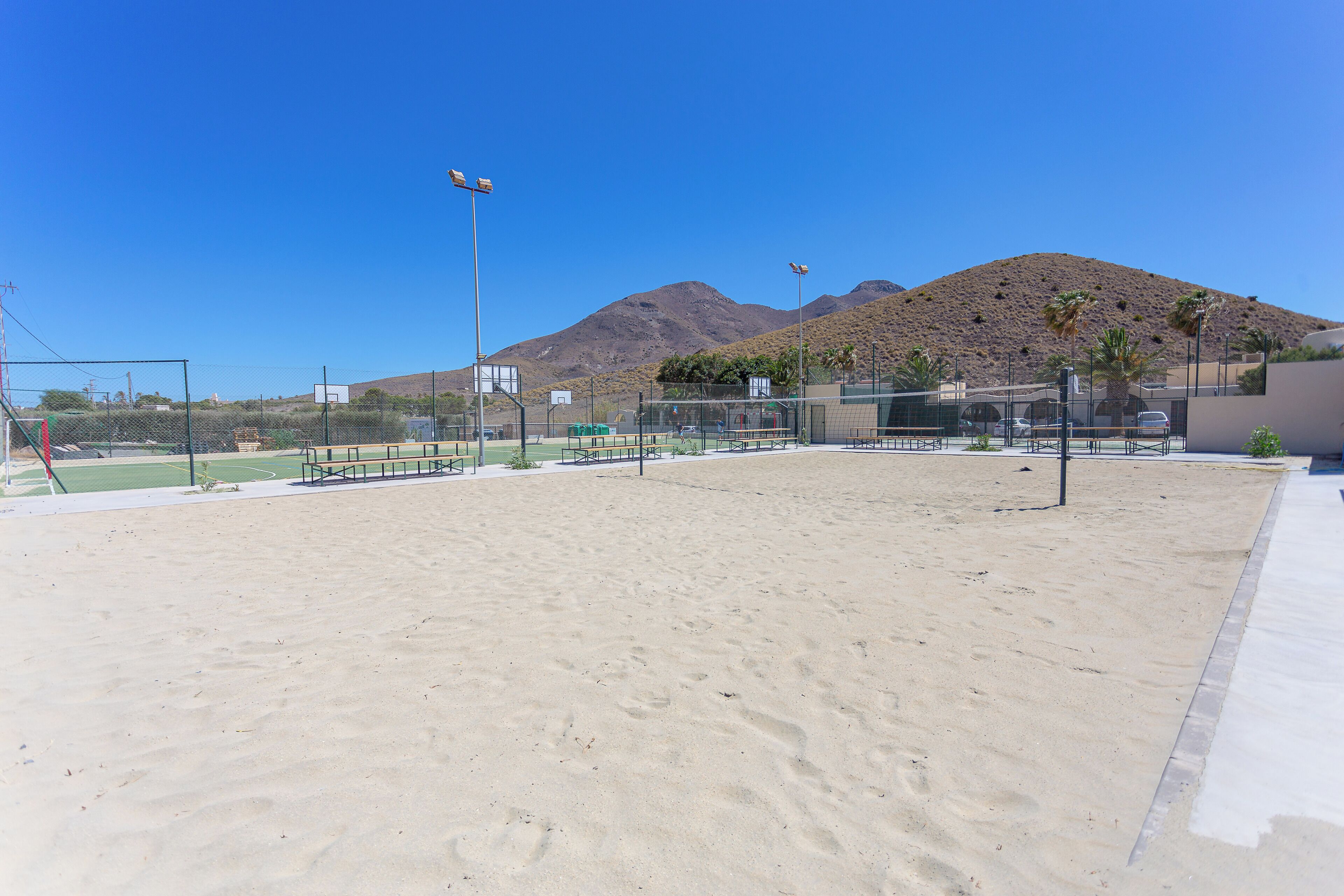 A sandy sports court with basketball hoops and a mountain in the background.