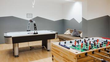 A room with a foosball table, a pool table, and a bed with a polka dot pillow.