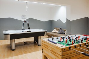 A room with a foosball table, a pool table, and a bed with a polka dot pillow.