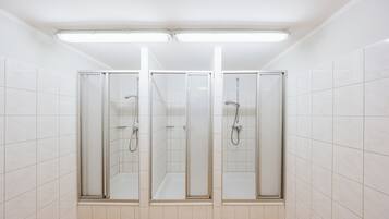 Un baño con tres cabinas de ducha con mampara de vidrio, paredes con azulejos blancos y suelo de madera.