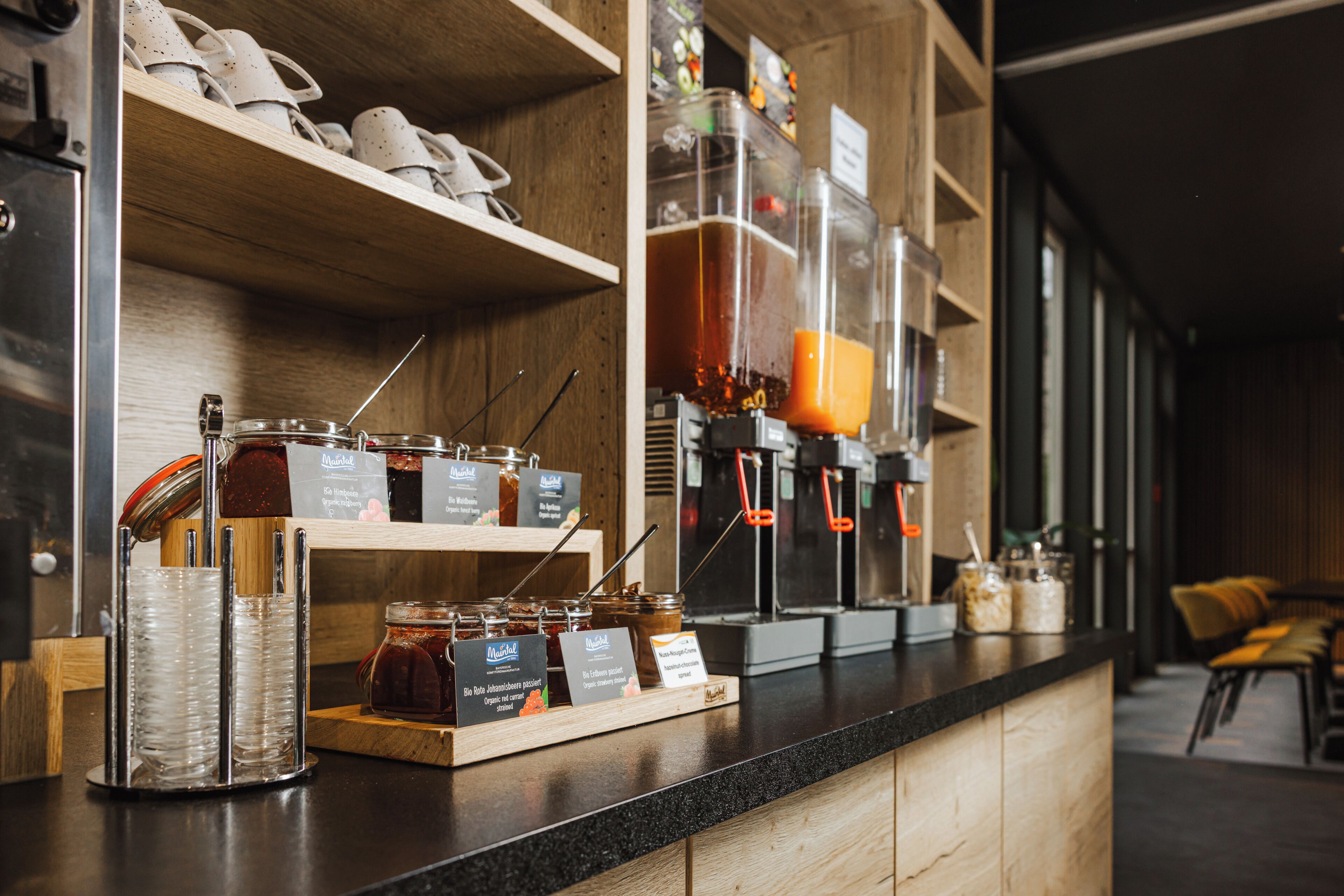 A coffee bar with jars of condiments, a coffee machine, and a display of cups.