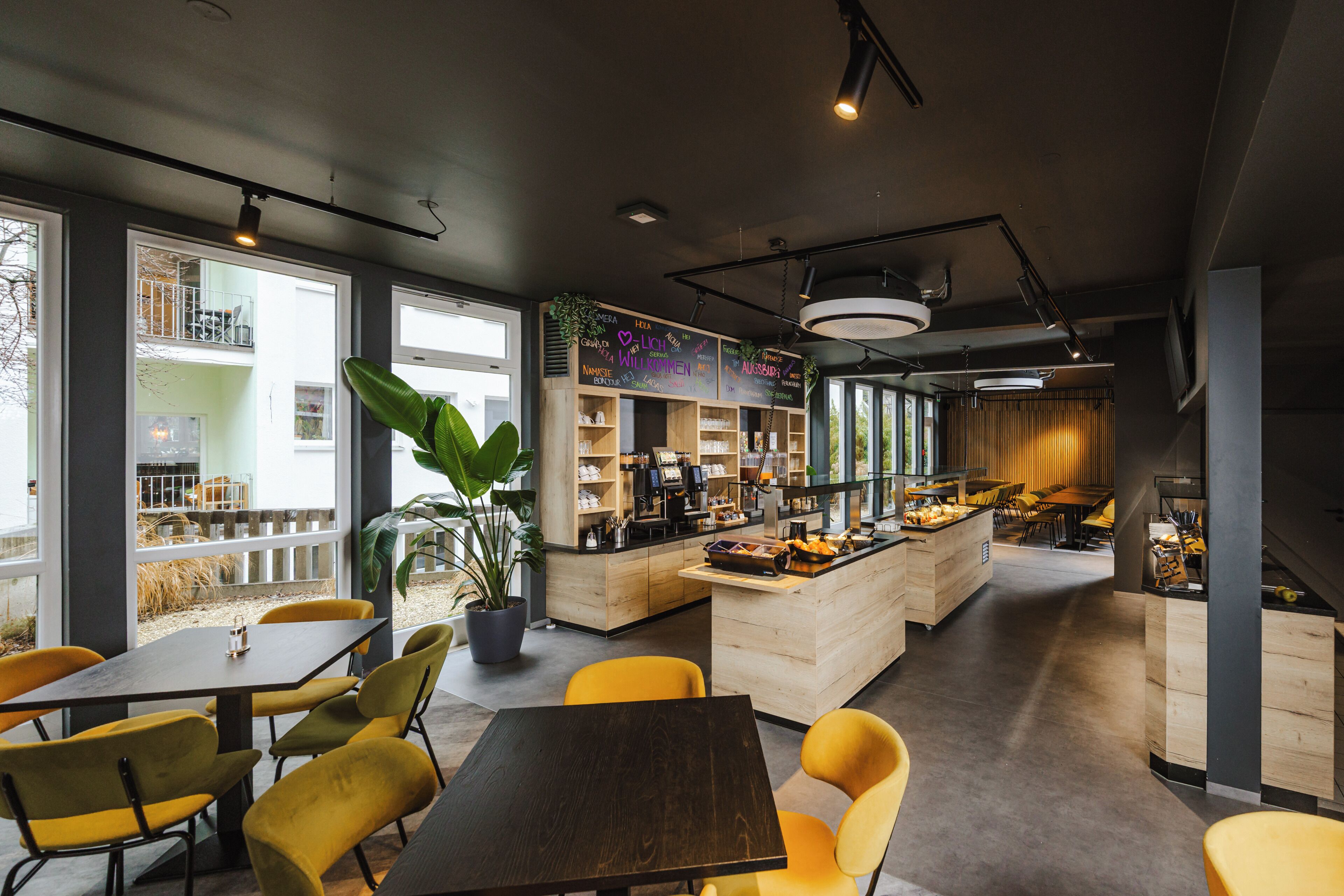 A modern cafe with yellow chairs, a wooden counter, and large windows.