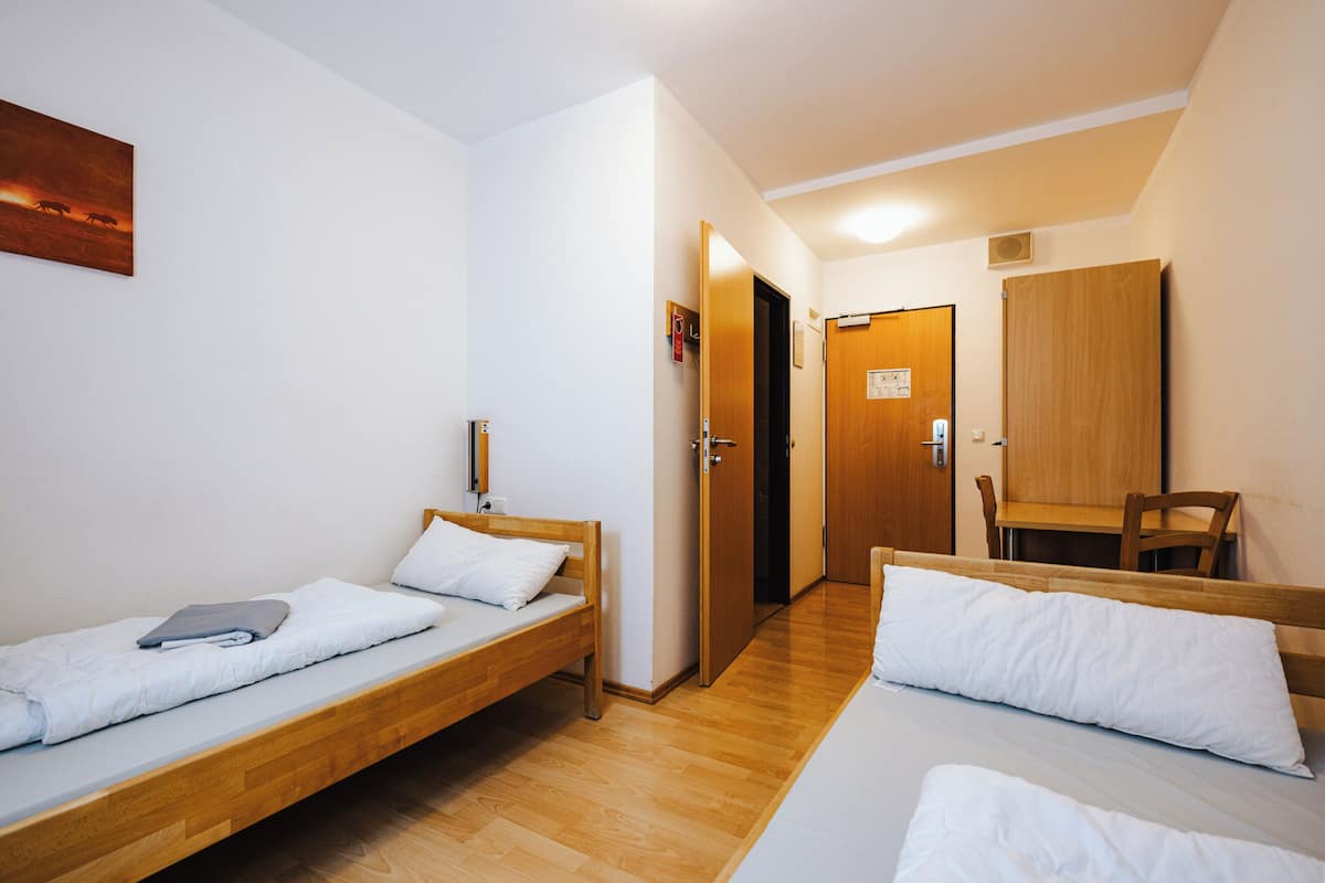 A room with two wooden beds, a wooden desk, a chair, and a door leading to another room.