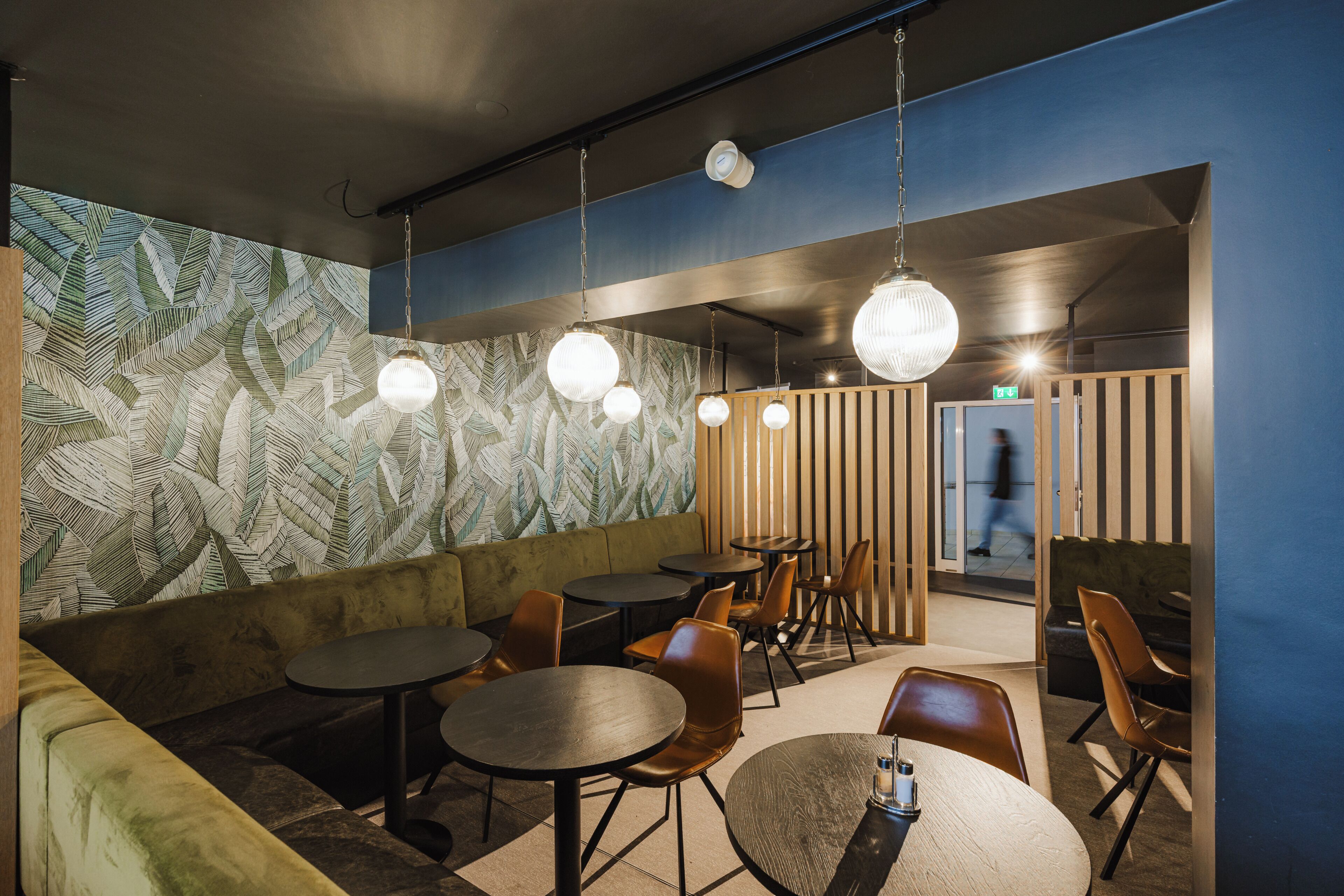 A restaurant interior with round tables, chairs, and hanging pendant lights.