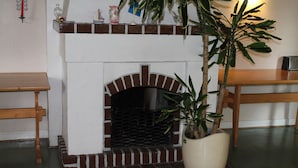 Una chimenea de ladrillo con repisa blanca, un banco de madera a la izquierda y una planta en maceta a la derecha.