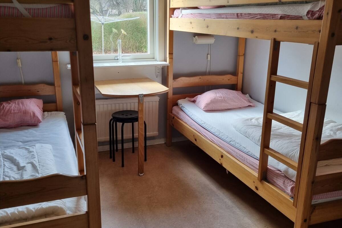 A dormitory room with bunk beds, a small desk, and a radiator.