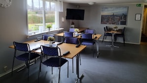 Un salón de conferencias con mesas y sillas, un reloj, un televisor y una ventana con vistas al exterior.