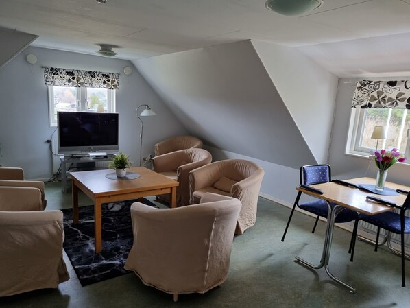 Una sala moderna con televisor de pantalla plana, sofás color beige, una mesa de centro de madera y un comedor con una mesa pequeña y sillas.