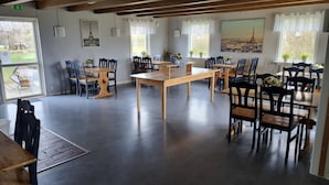 Un comedor amplio con mesas y sillas de madera, ventanas grandes con cortinas y obras de arte que representan lugares emblemáticos.