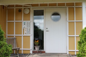 Eine weiße Tür mit rundem Fenster, einem Schild mit der Aufschrift "Valkommen" und einem an der Wand montierten Stromverteiler.