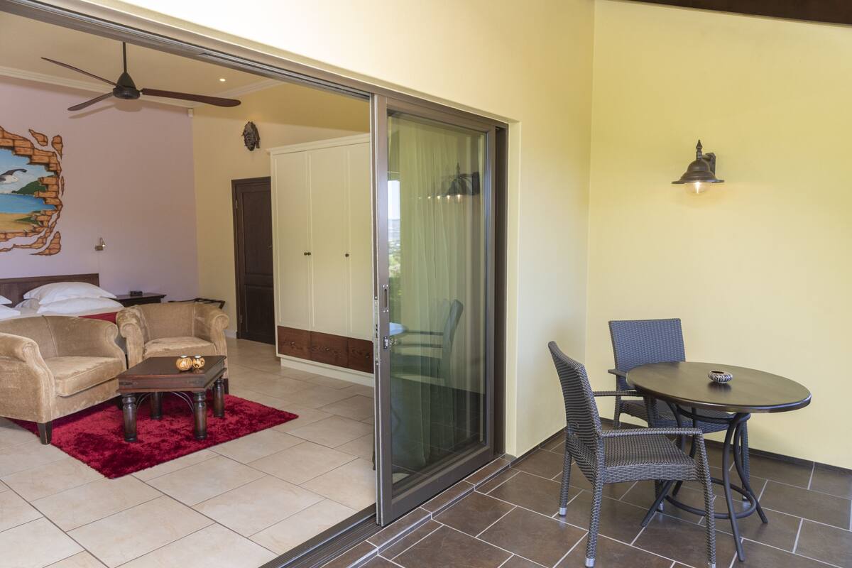A room with a sliding glass door leading to a balcony, a sofa, a small table with decorative items, and a wicker chair.