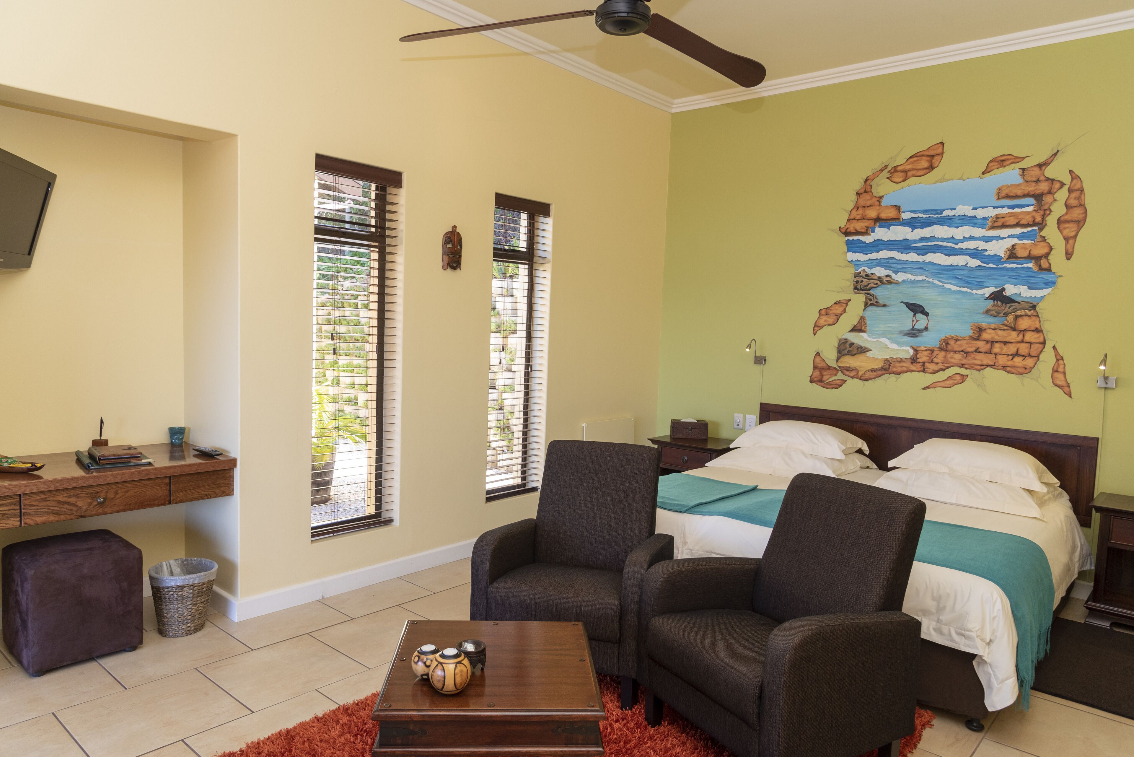 A bedroom with a bed, two armchairs, a desk, and a TV.