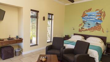 A bedroom with a bed, two armchairs, a desk, and a TV.