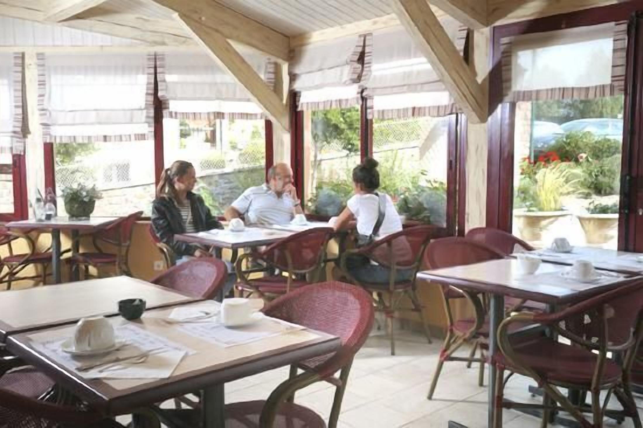 A covered outdoor café with tables and chairs, surrounded by windows with views of greenery.