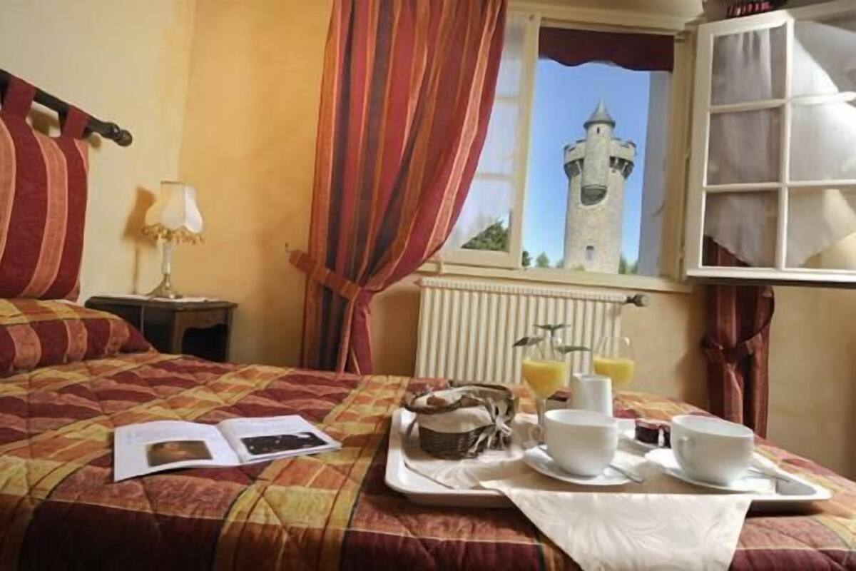 A hotel room with a bed, a tray with breakfast items, a window with a view of a tower, and curtains.