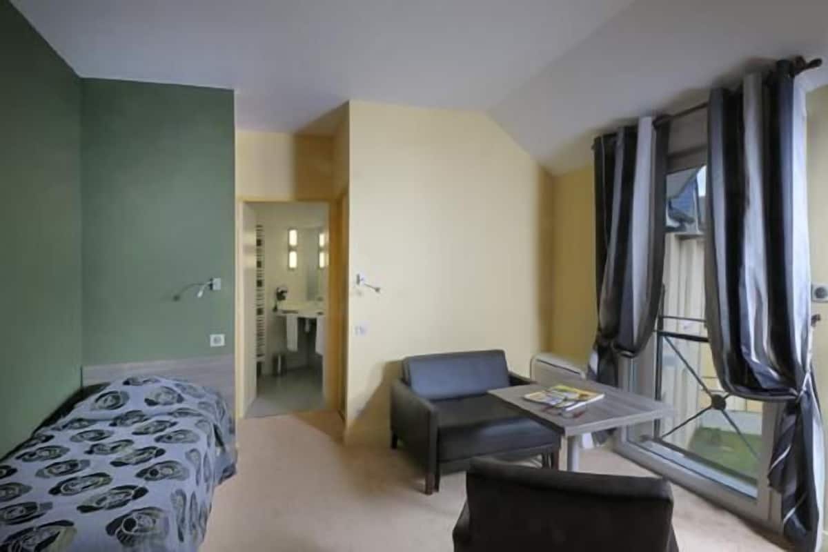 A hotel room with a bed, a desk, a chair, and a window with curtains.