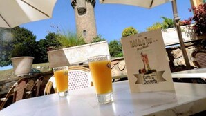 A table with two glasses of orange juice, a menu titled "Hotel de la Tour," and a stone tower in the background. - Hôtel-Restaurant de la Tour (Masseret)