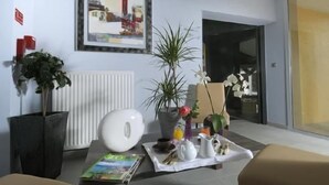 A modern living room with a white radiator, a framed painting, a potted plant, a coffee table with a magazine, and a breakfast tray. - Hôtel-Restaurant de la Tour (Masseret)