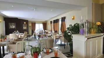 A hotel dining area with tables set for guests, a reception desk, and a view of the cityscape.