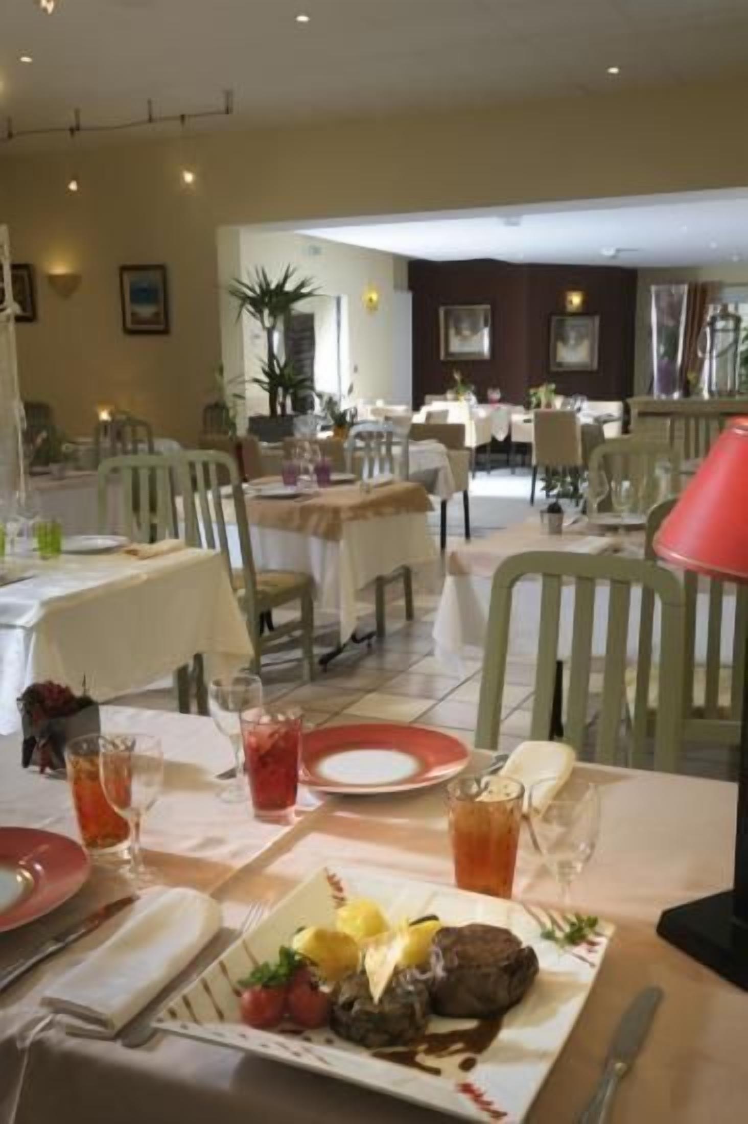 A dining area with tables set for meals, chairs, and a table lamp.