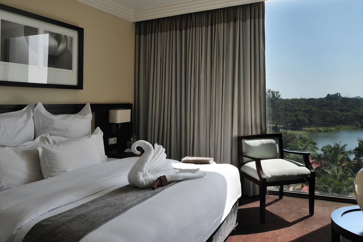 A hotel room with a bed, a chair, a desk, a lamp, and a view of a lake.