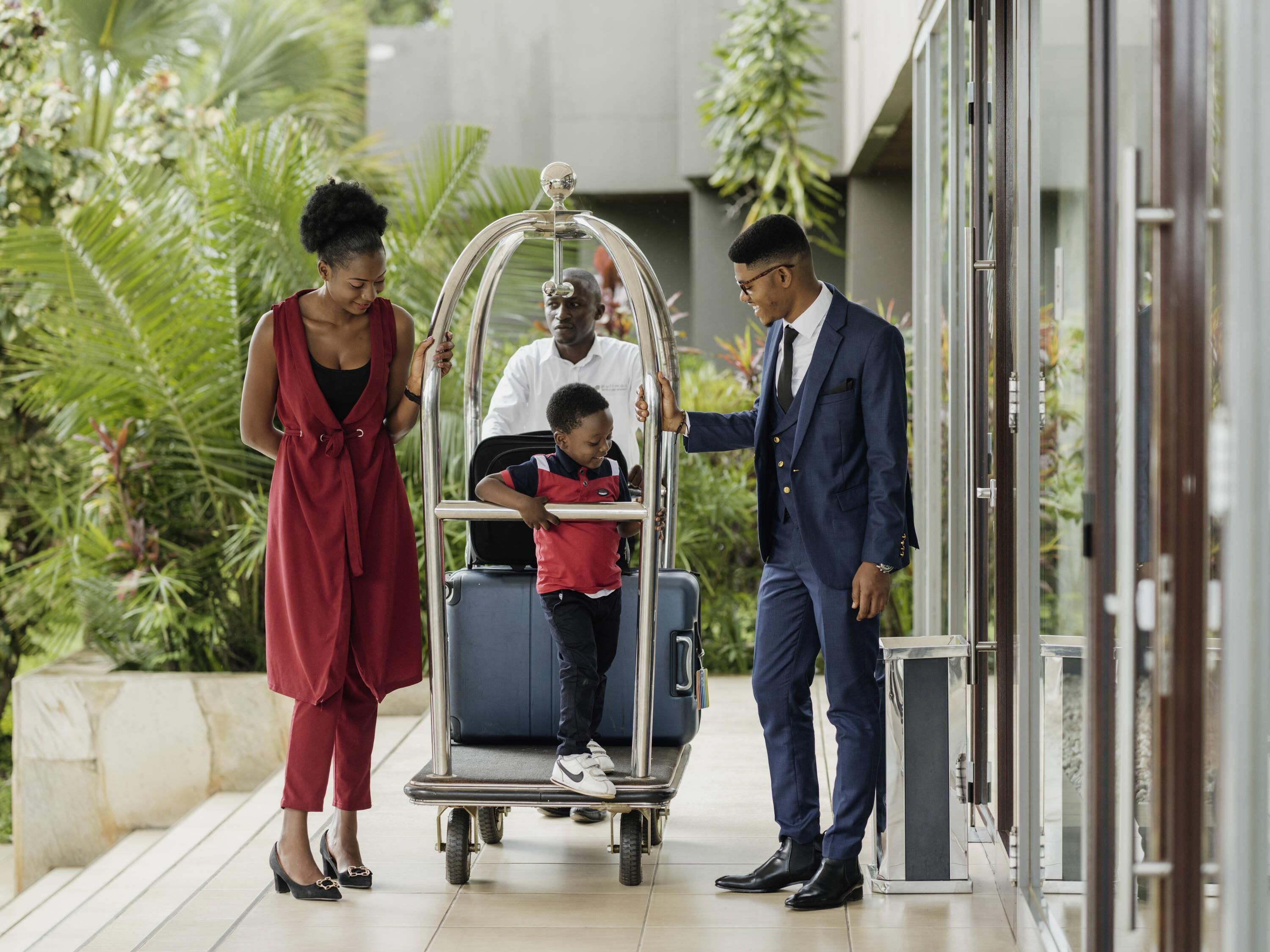 Una familia subiendo equipaje a un carrito en un pasillo de hotel con vegetación y arquitectura moderna.