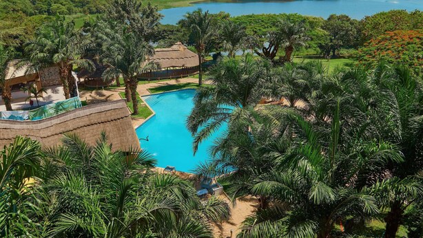 A resort with a swimming pool surrounded by palm trees and a view of a lake. - Hotel Pullman Lubumbashi Grand Karavia (Lubumbashi)
