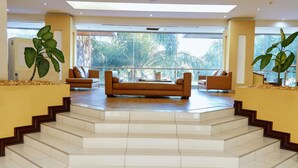 A modern interior with a staircase leading to a balcony, featuring a sofa set and large windows. - Hotel Pullman Lubumbashi Grand Karavia (Lubumbashi)