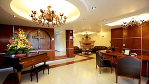 Un hall d’entrée avec un grand piano, un comptoir d’accueil et une croix accrochée au mur.