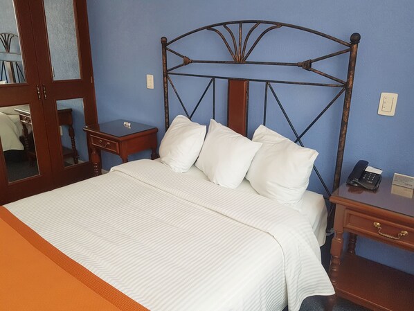 A neatly made bed with white bedding and pillows, a wooden headboard, a bedside table with a phone and a notepad, and a mirror on the wall. - Hotel Ciros (Pachuca)