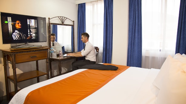 Une chambre d’hôtel avec un lit, un bureau avec un ordinateur portable, une télévision et un miroir.