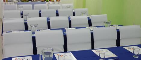 A conference room with rows of white chairs, blue tablecloths, and name cards.
