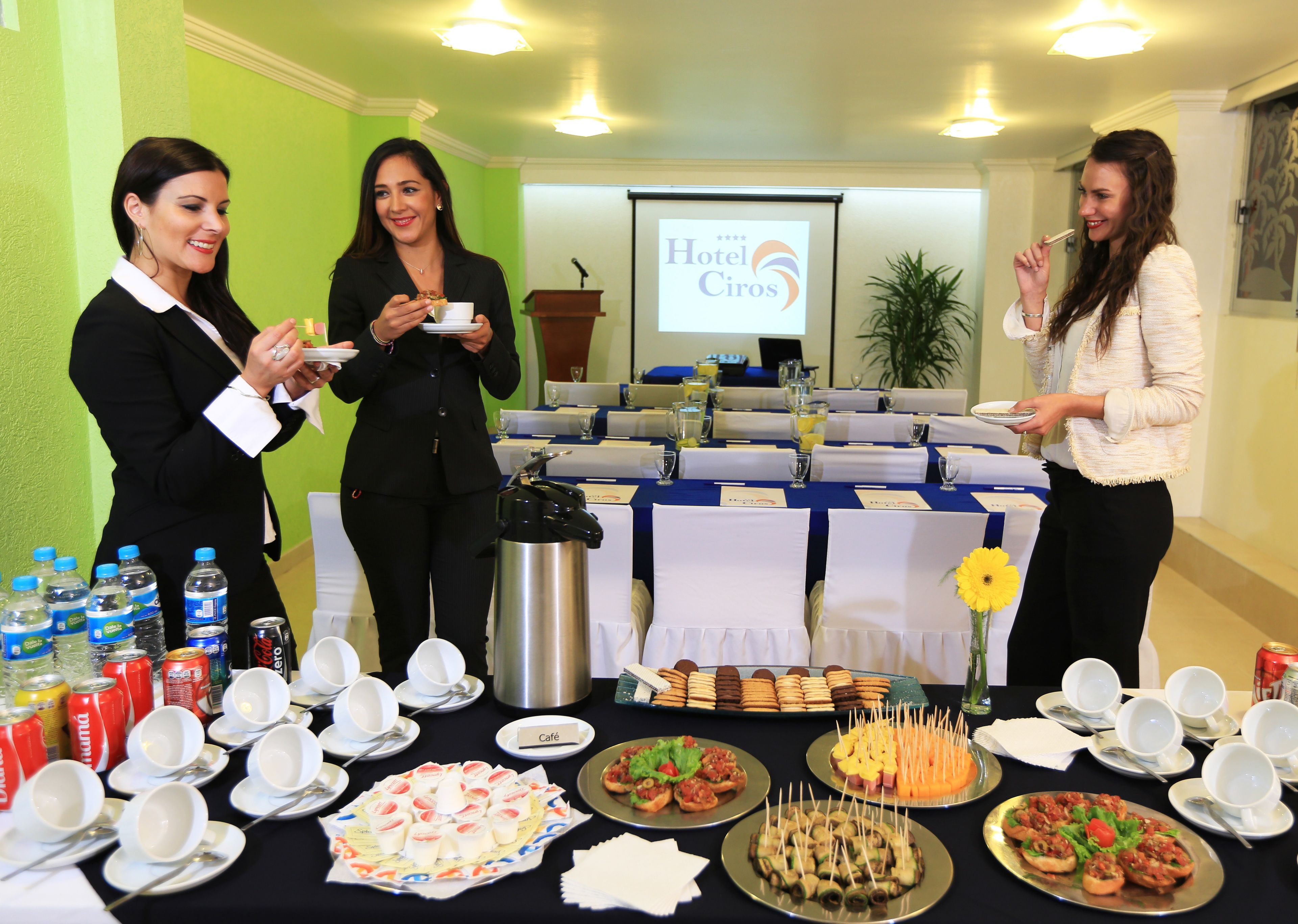 A buffet setup with various food items and beverages, a podium, and a presentation screen in the background.