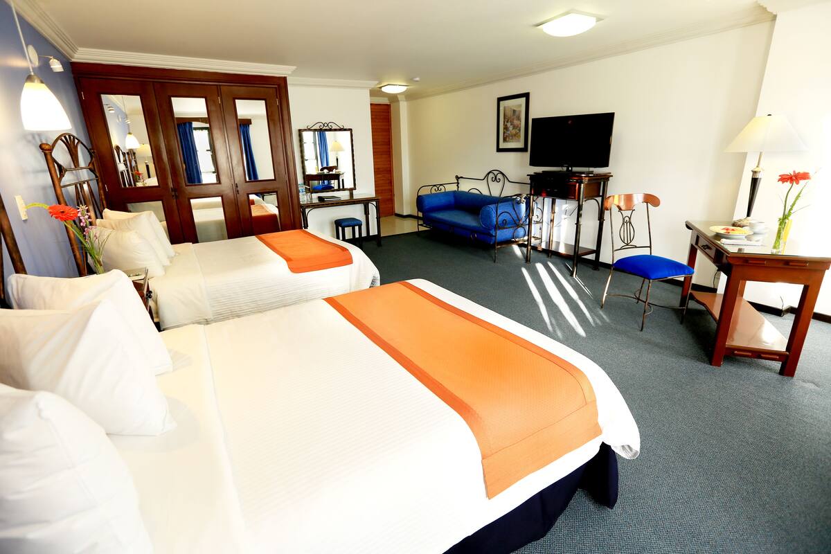 A hotel room with two beds, a desk, a television, and a sofa.