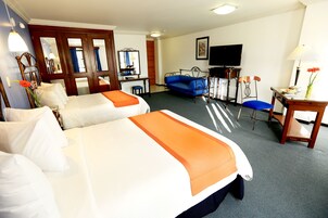 Quarto de hotel com duas camas, uma escrivaninha, televisão e sofá.