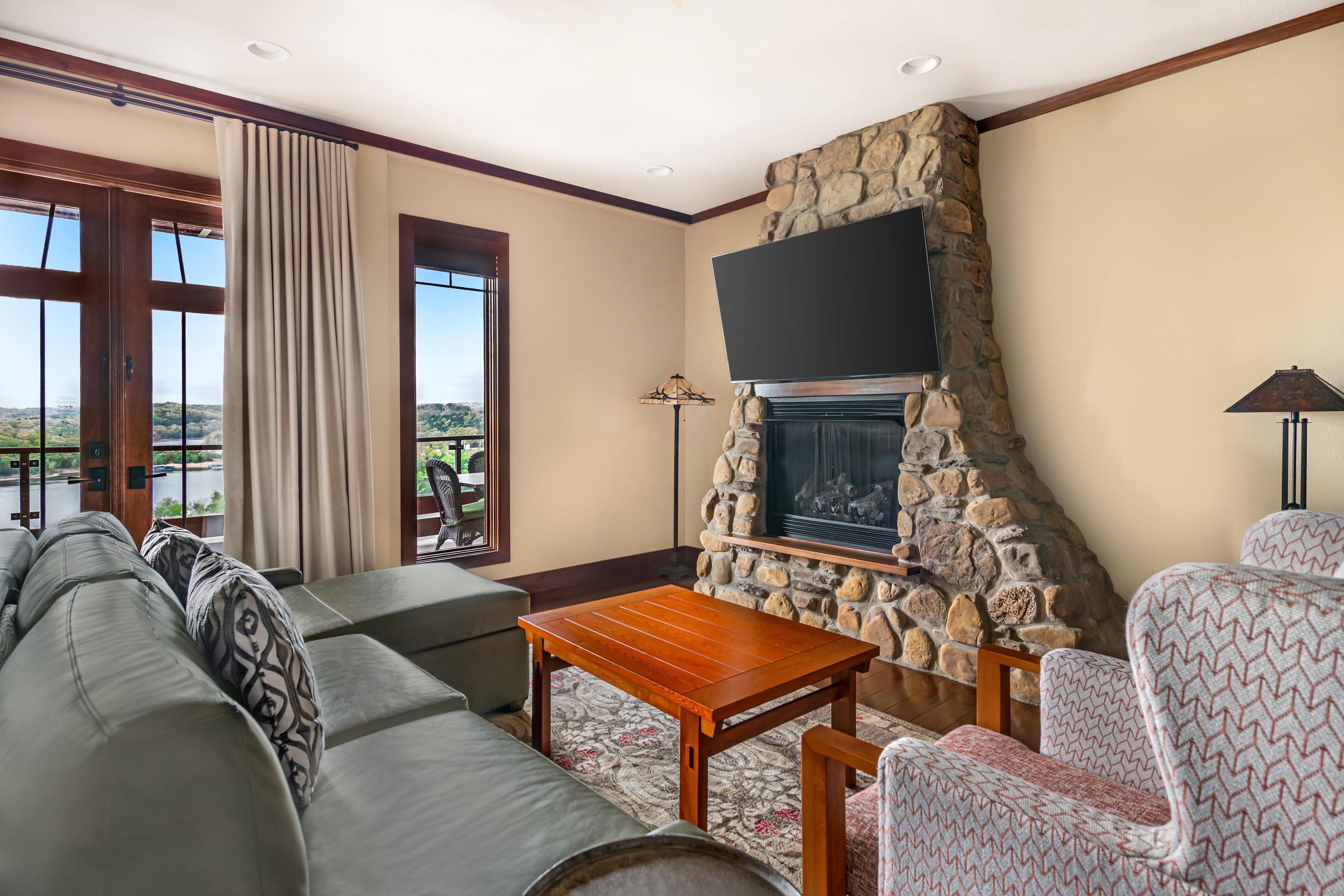 Una sala de estar con chimenea de piedra, televisor de pantalla plana, sofá y sillas estampadas.