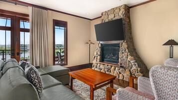 Una sala de estar con chimenea de piedra, televisor de pantalla plana, sofá y sillas estampadas.
