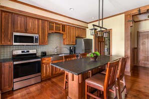 A kitchen with wooden cabinets, a stainless steel oven, a microwave, a refrigerator, and a dining table with chairs. - Hilton Grand Vacations Club Long Creek Ridgedale (Ridgedale)