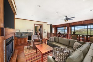 Amplia sala de estar con chimenea, muebles de madera, balcón con vistas y zona de cocina.