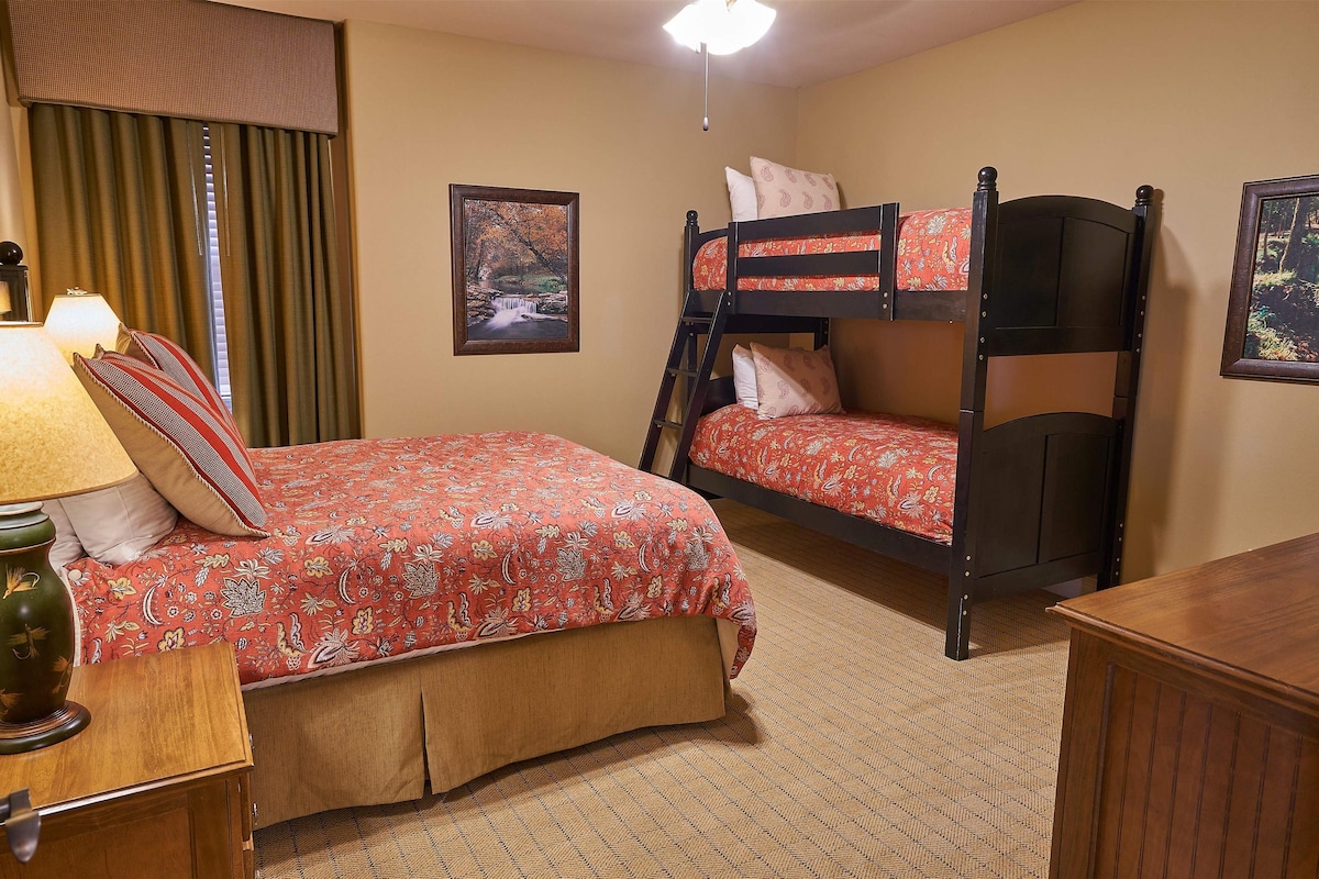 A room with a bunk bed, a desk with a lamp, and a framed picture on the wall.