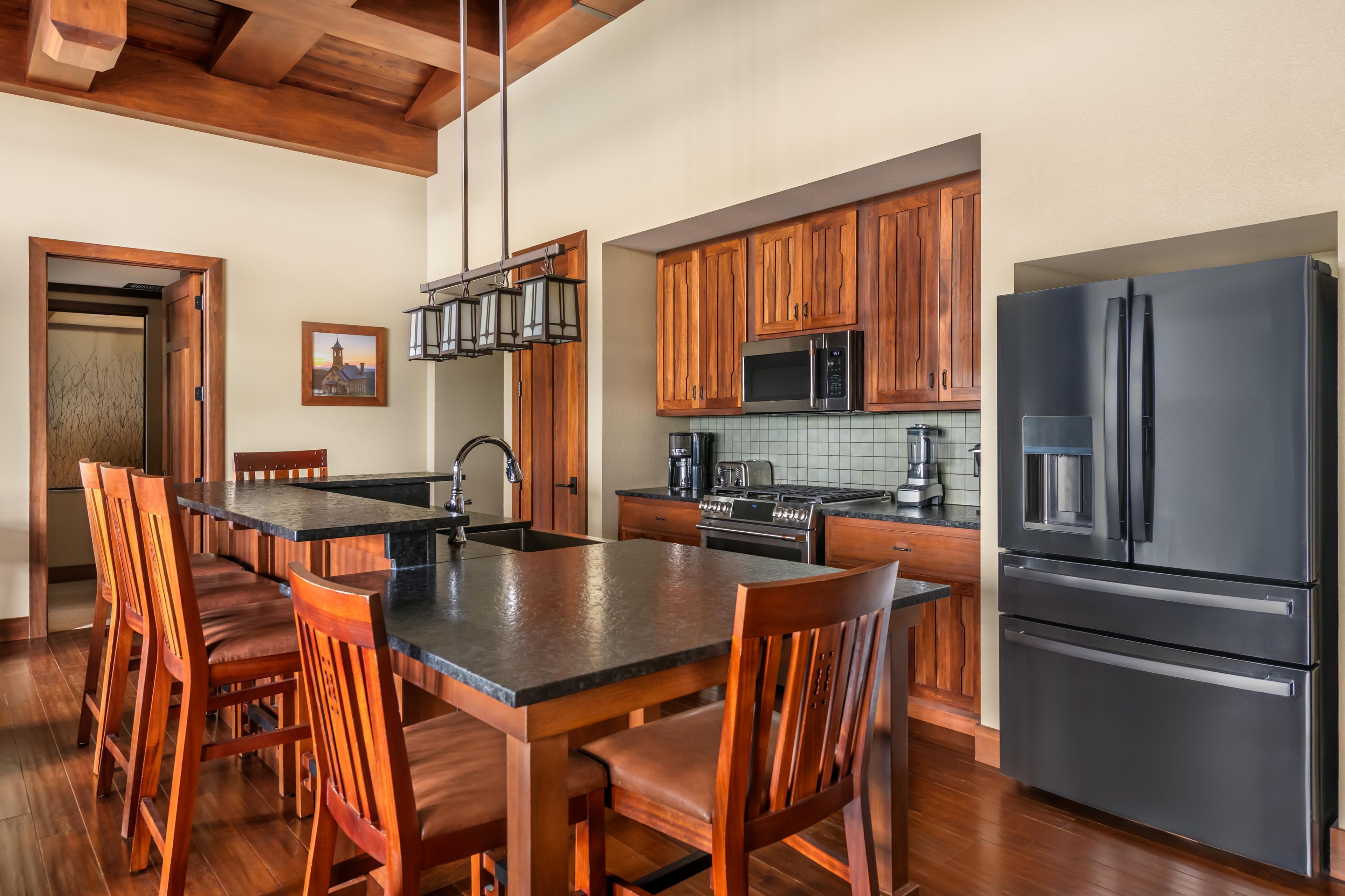 Una cocina con armarios de madera, un refrigerador negro y un comedor con sillas de madera y una mesa negra.