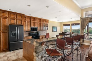 Una cocina con armarios de madera, un refrigerador negro, una isla de piedra y un comedor con sillas y mesa.