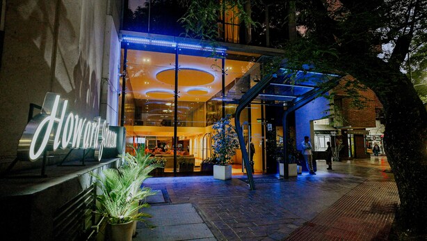 A hotel entrance with a glass facade, a sign reading "Howard Johnson," and a blue-lit entrance canopy.