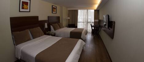 A hotel room with two beds, a desk, a chair, a TV, and a window with curtains.