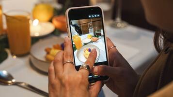 A person holding a smartphone, possibly taking a photo or video of a dining table with a glass of orange juice and a plate of food.