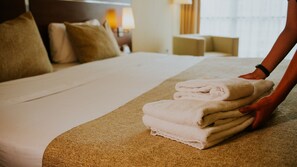 A neatly made bed with a folded towel stack and a person placing the towels. - Howard Johnson by Wyndham Córdoba La Cañada (Córdoba)